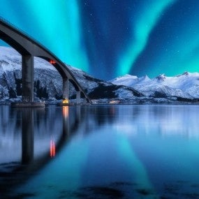 Bridge and aurora borealis over snowy mountains. Lofoten islands